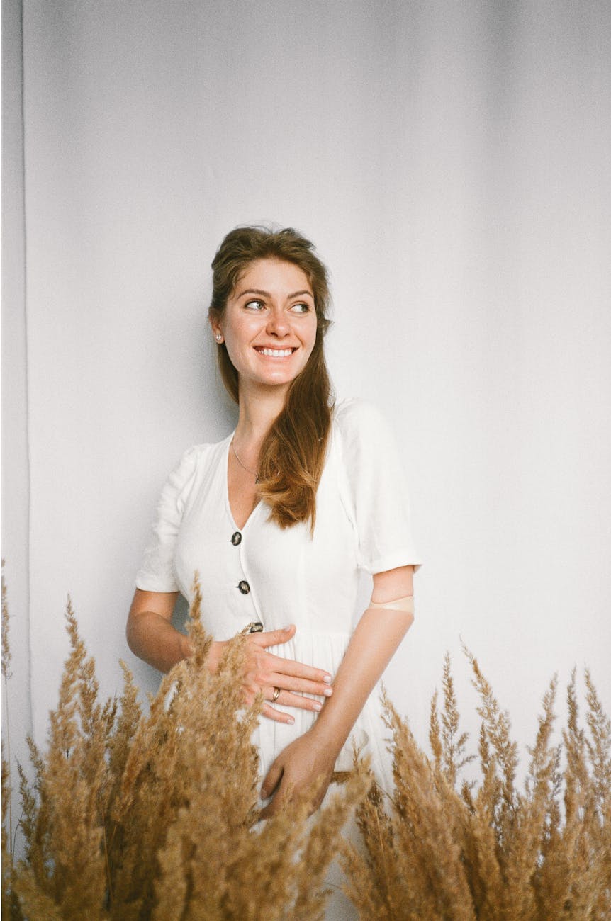 woman in white dress standing behind dried grass