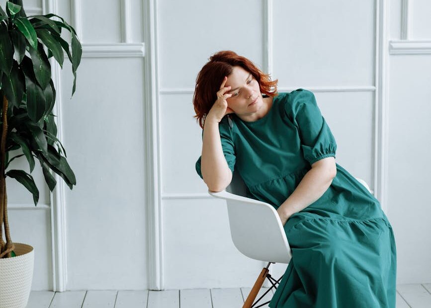 woman in green dress sitting on a chair while in deep thoughts